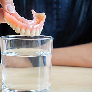 person putting dentures in water