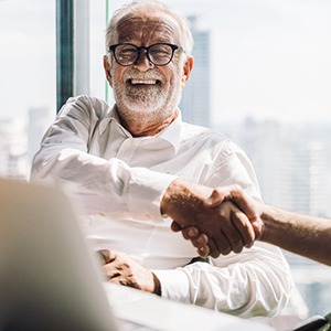An older businessman smiling and shaking someone’s hand
