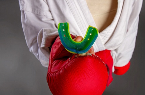 Hand in boxing glove, holding mouthguard for sports
