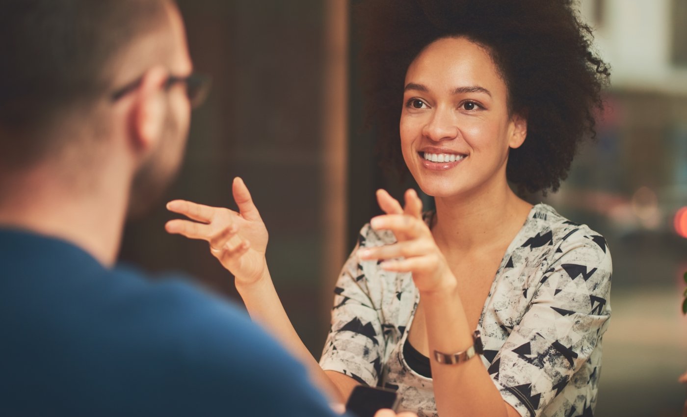 Woman talking to man sitting across from her at a desk