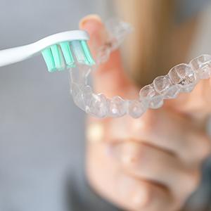 Closeup of patient cleaning clear aligner with toothbrush